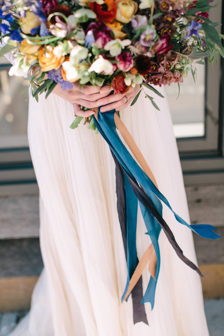 Bouquet of flowers held by a person wearing a white dress with colorful ribbons.
