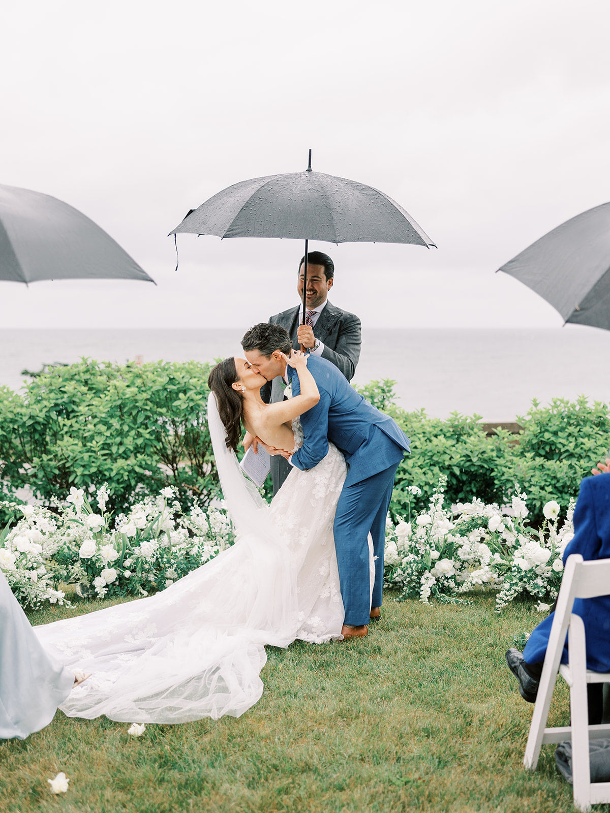 Wedding couple sharing a kiss with guests holding umbrellas outdoors.