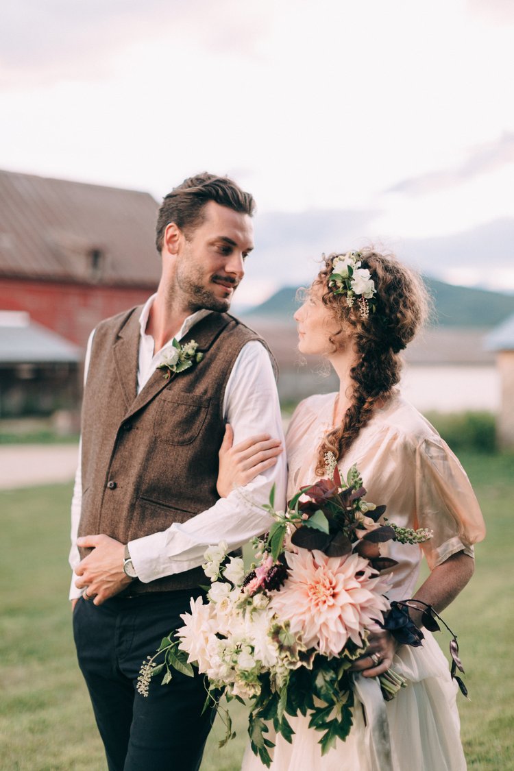 Couple in wedding attire standing outdoors with a rustic background