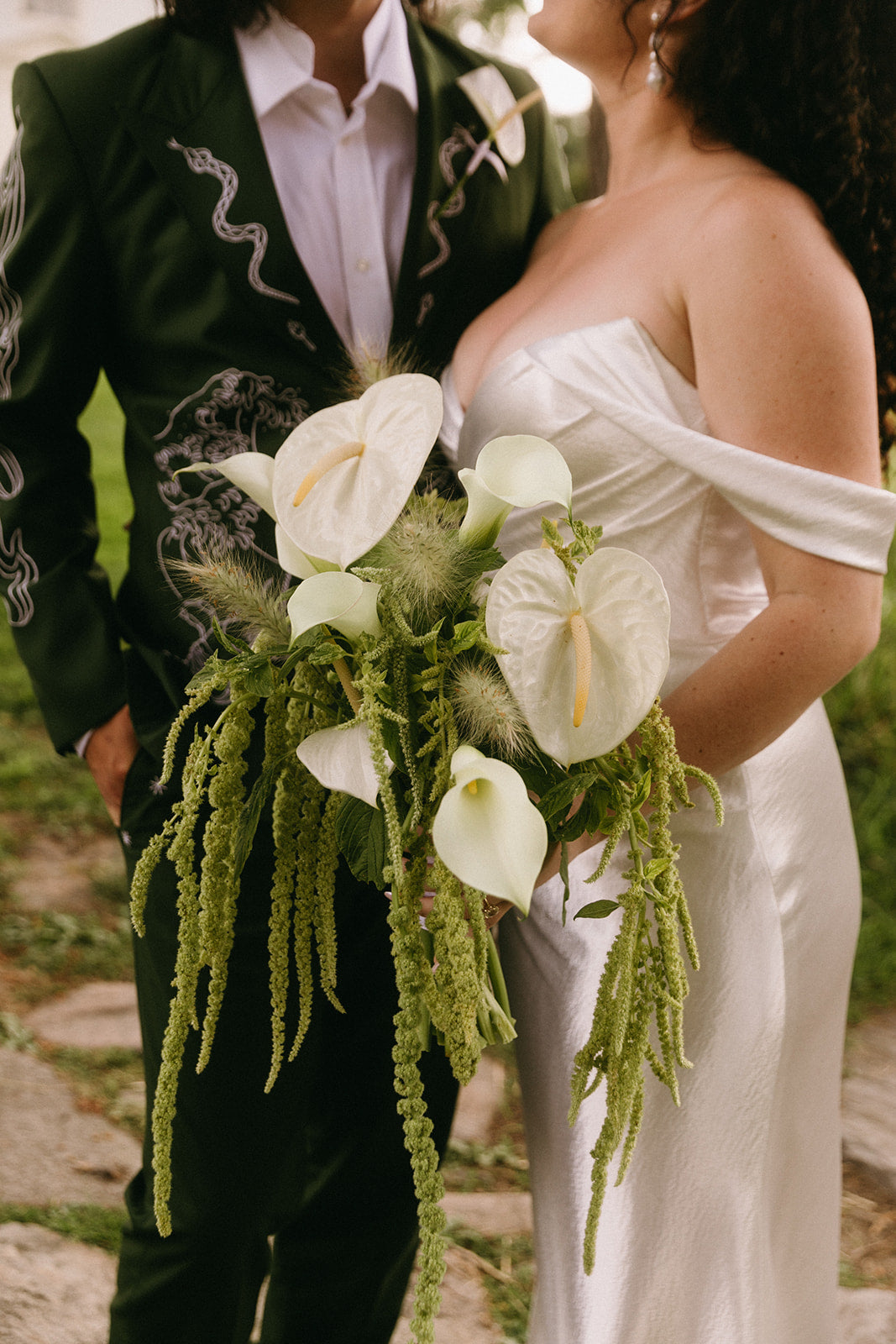 Bride holding a bouquet with white flowers and greenery, standing next to a person in formal attire.