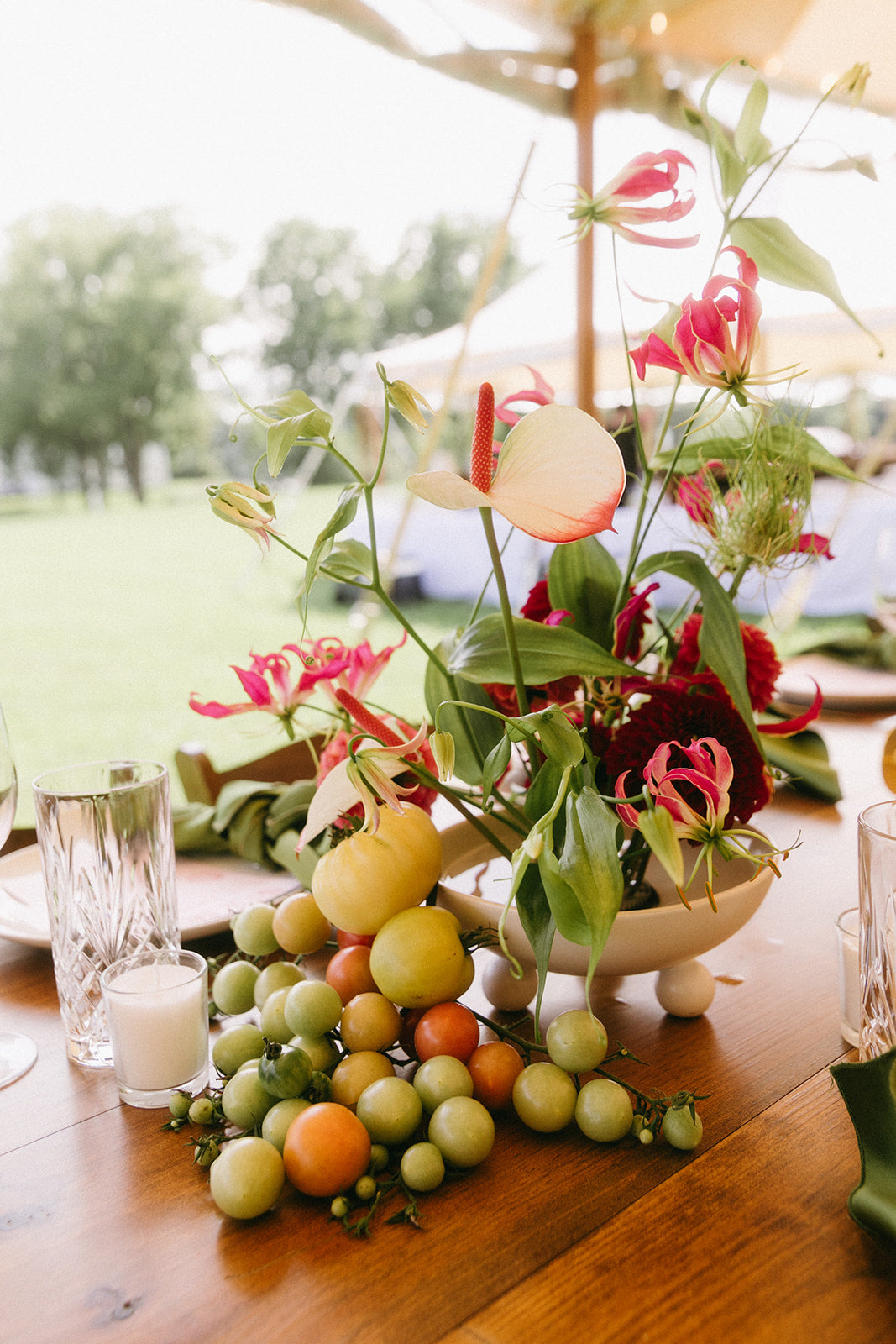 Decorative centerpiece with flowers and fruits on a wooden table outdoors.