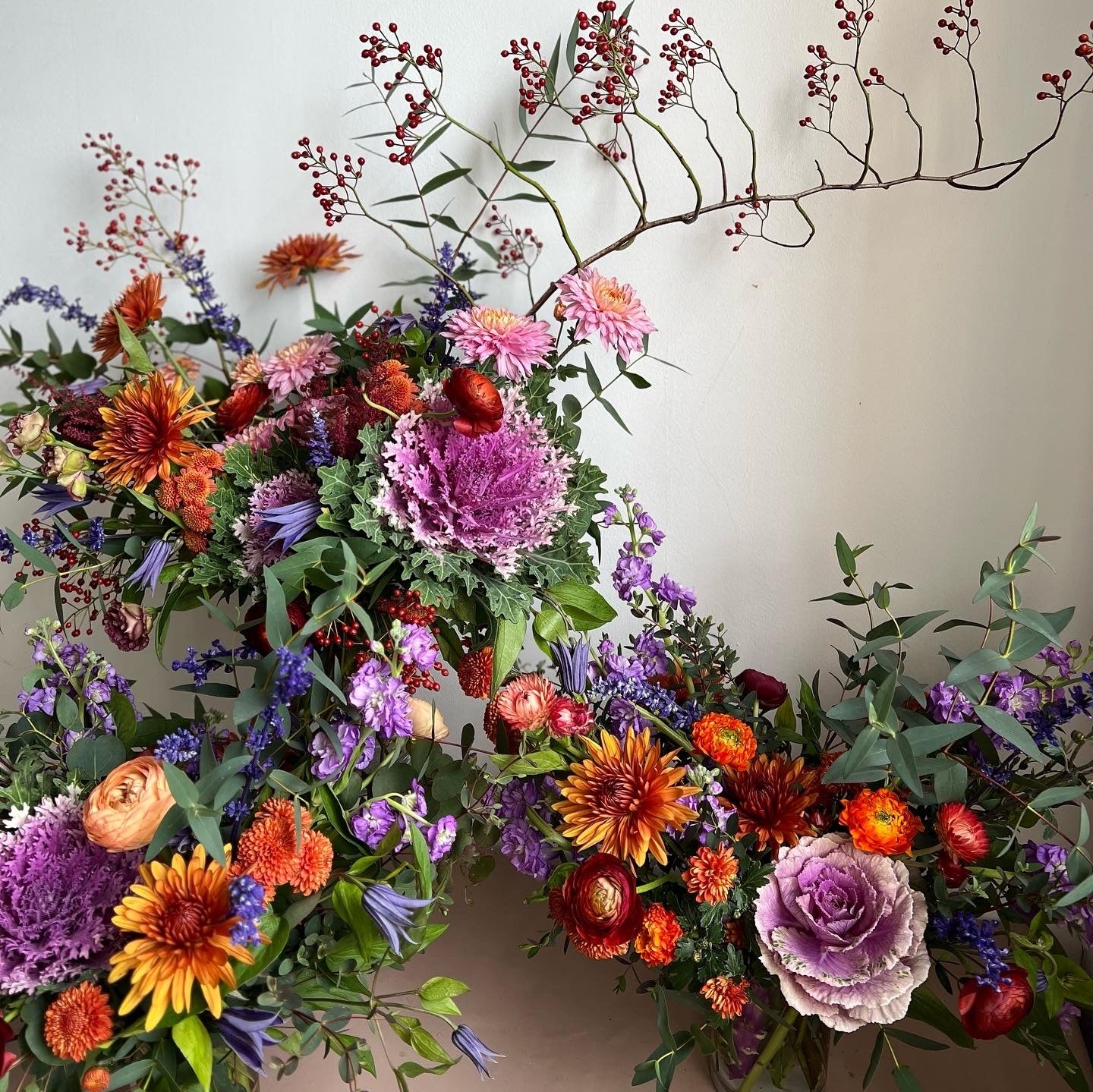 Colorful floral wreath with various flowers and greenery on a plain background