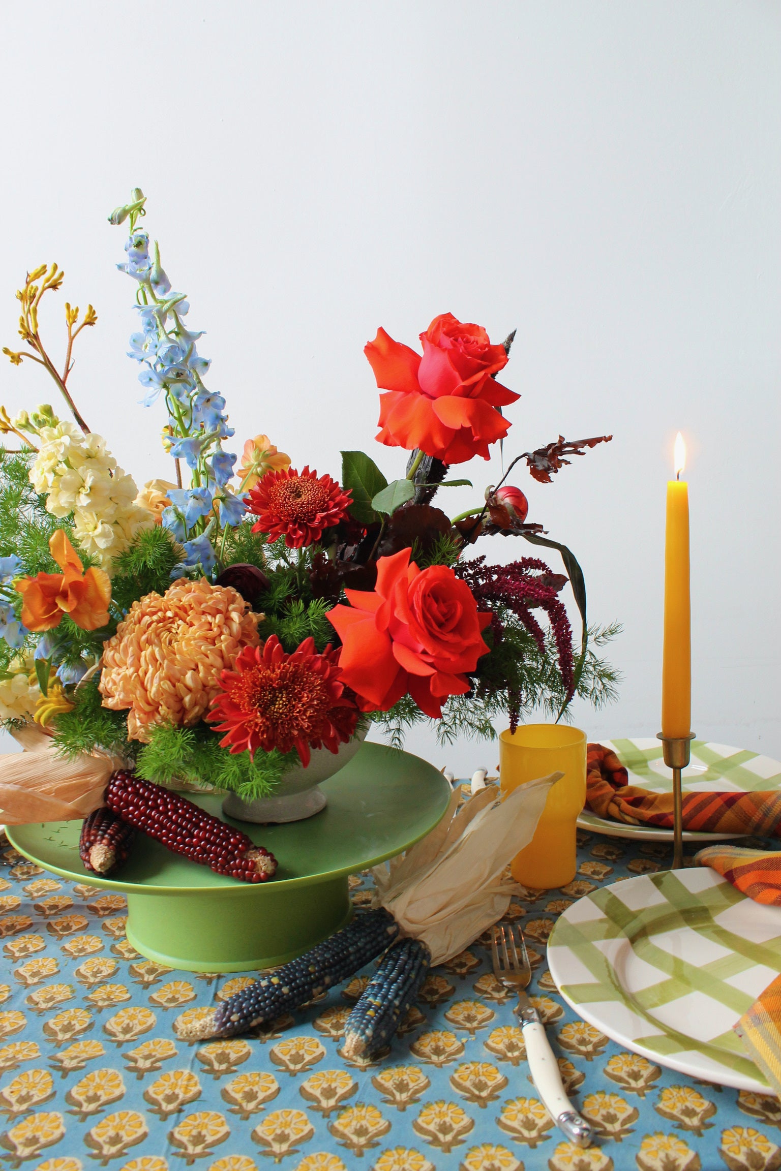 Colorful floral arrangement on a table with a candle and plates.
