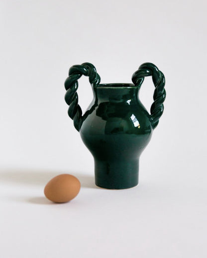 Green vase with twisted handles next to a brown egg on a white background