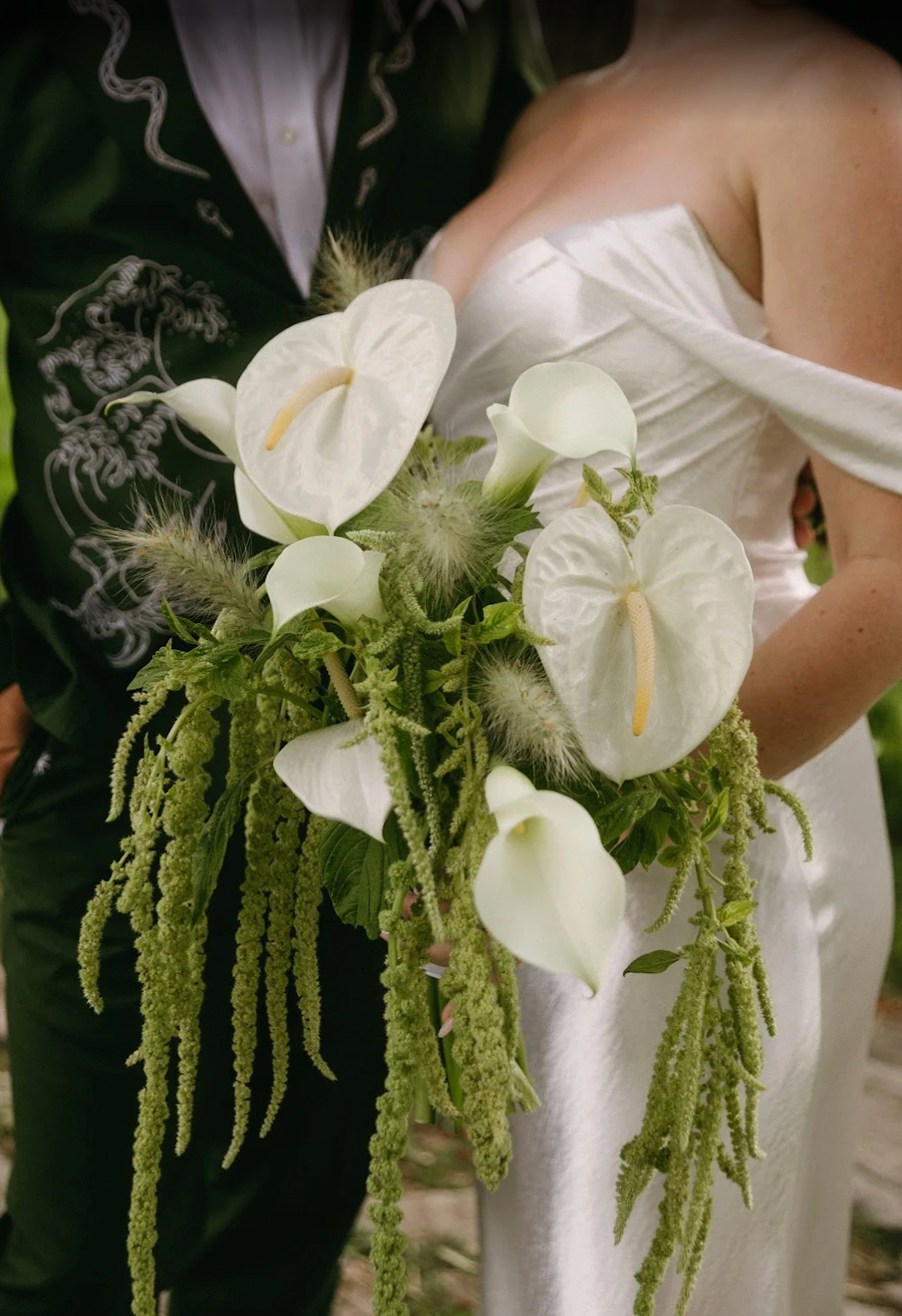 Bouquet with white flowers and greenery held by a person in a white dress.