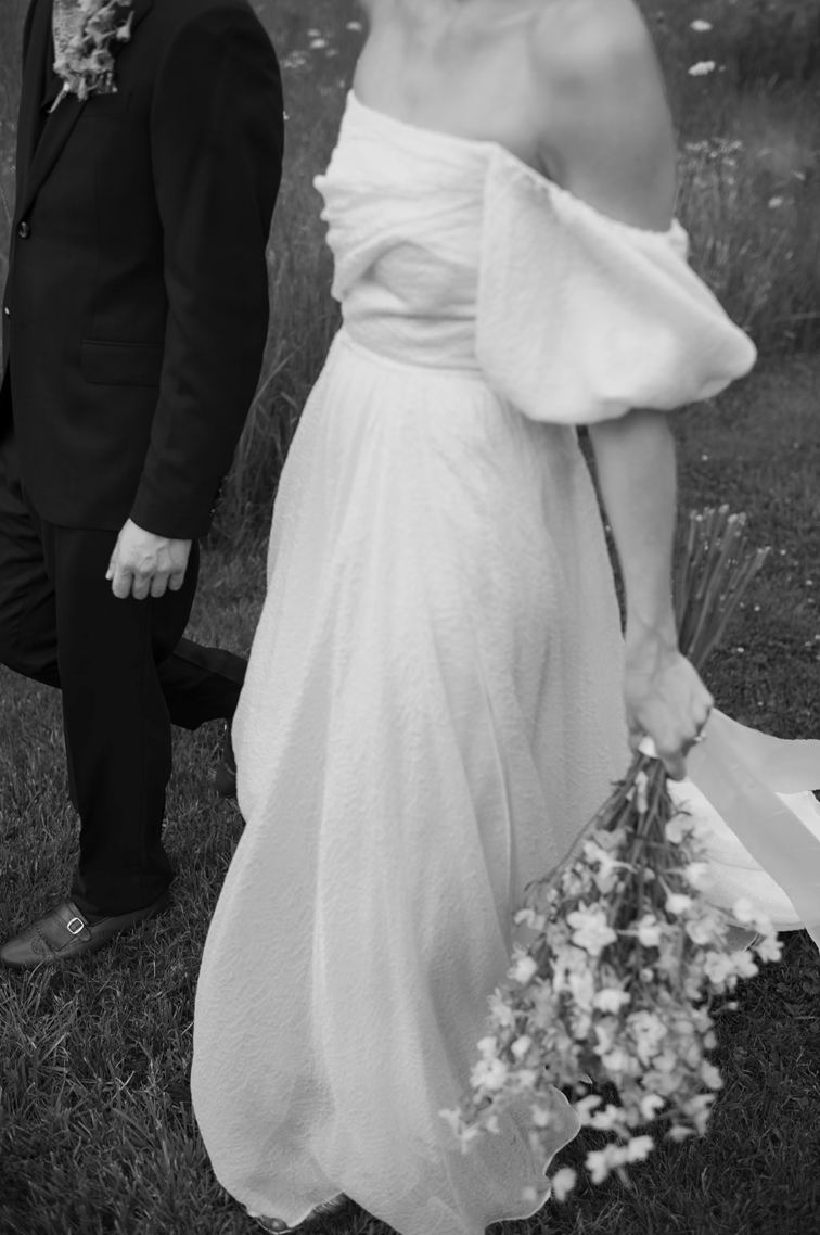 Black and white photo of a person in a wedding dress holding flowers, with another person in formal attire partially visible.