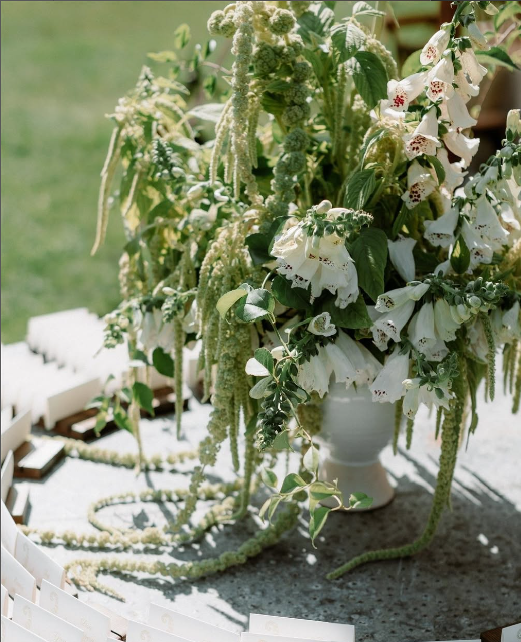 Decorative floral arrangement with white flowers and greenery on a table outdoors.