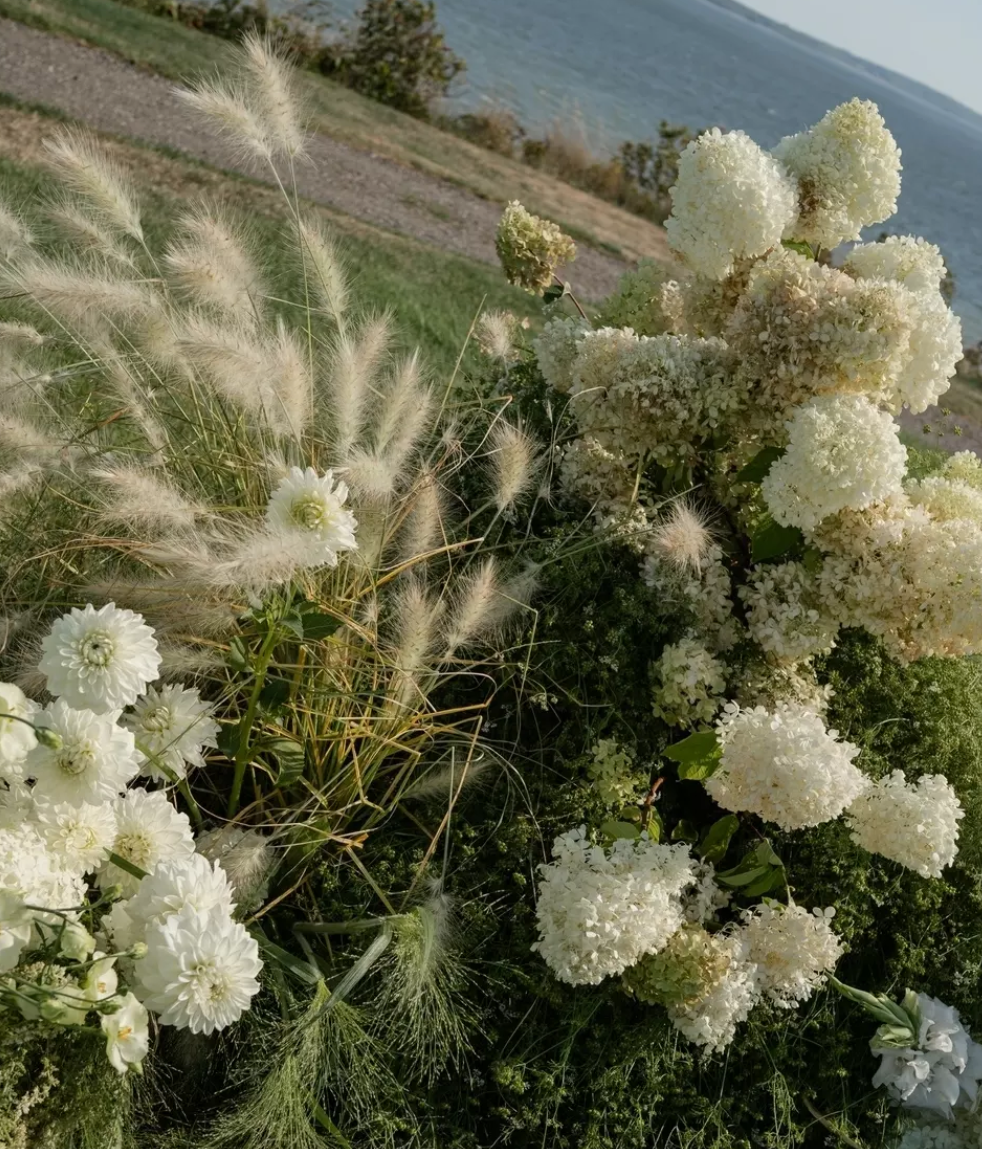 Floral arrangement with white flowers and greenery by a body of water