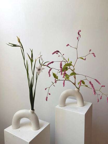 Two modern white vases with handles holding plants on a plain background