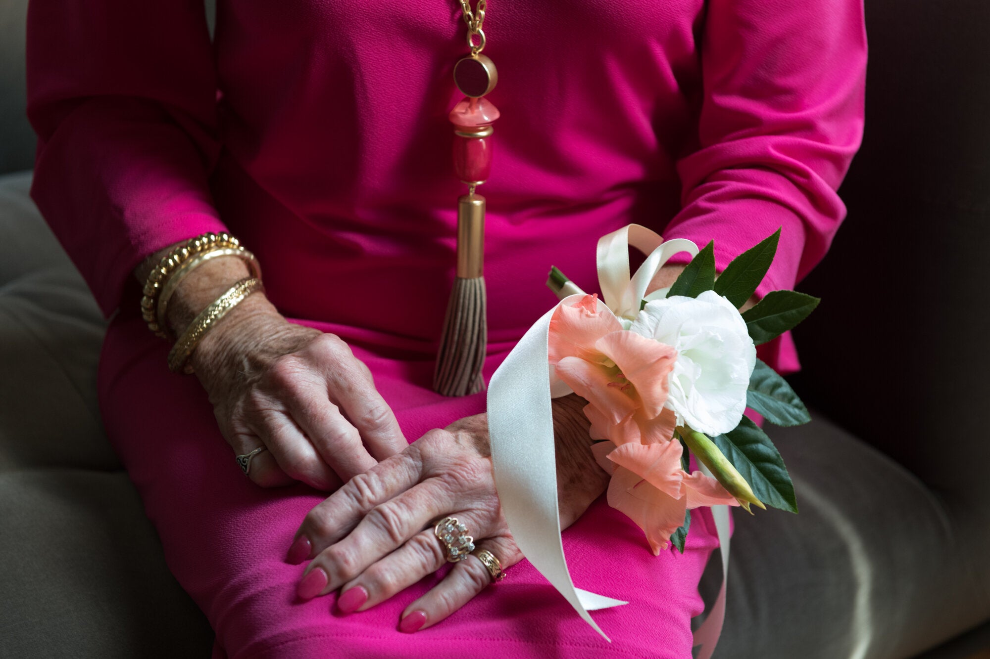 Person wearing a pink outfit with a floral corsage on a dark background