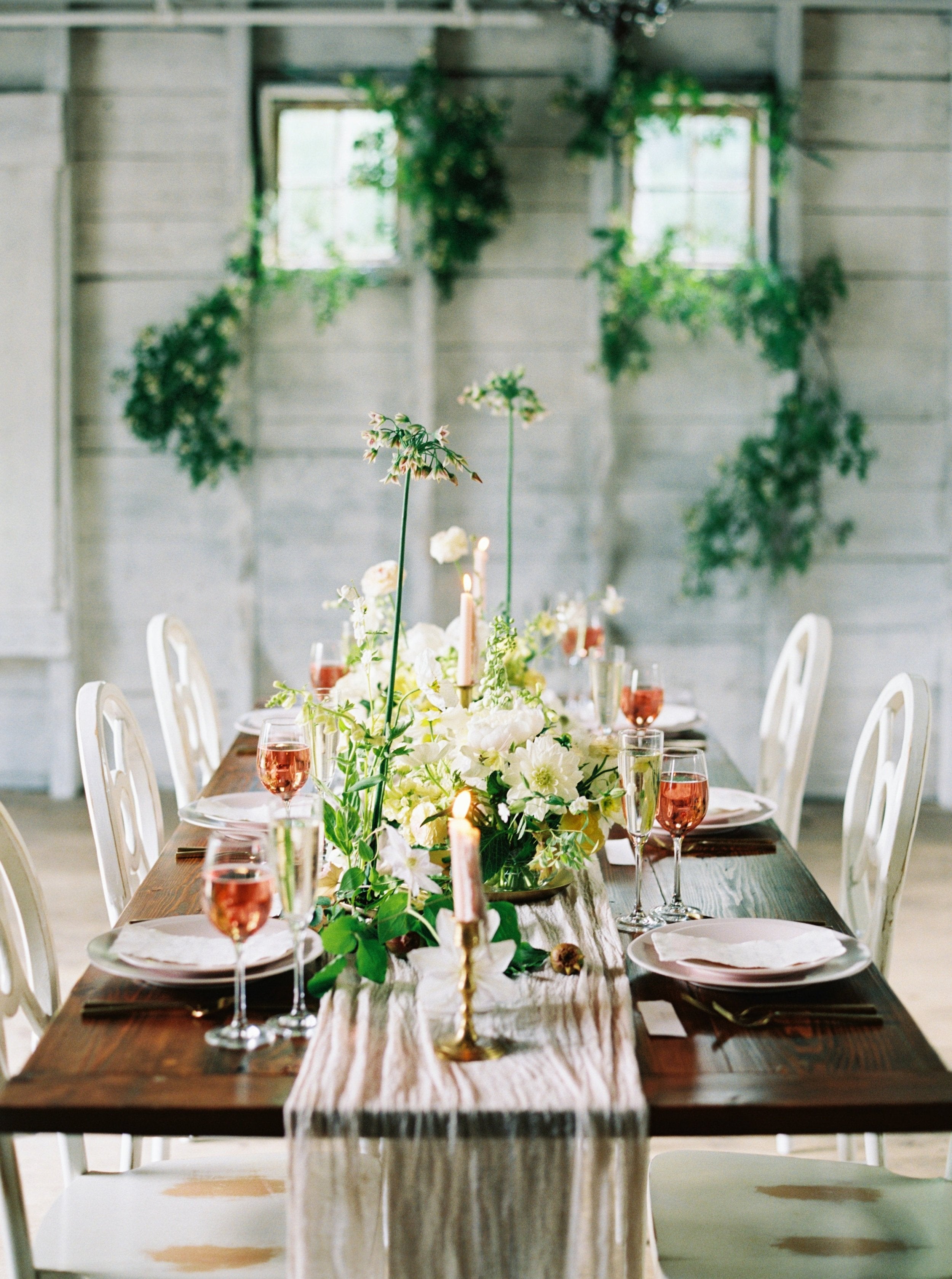 Elegant dining table setting with flowers, candles, and glasses in a rustic room.