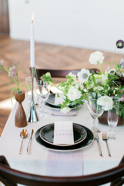 Elegant table setting with black plates, silverware, and floral arrangements on a white tablecloth.