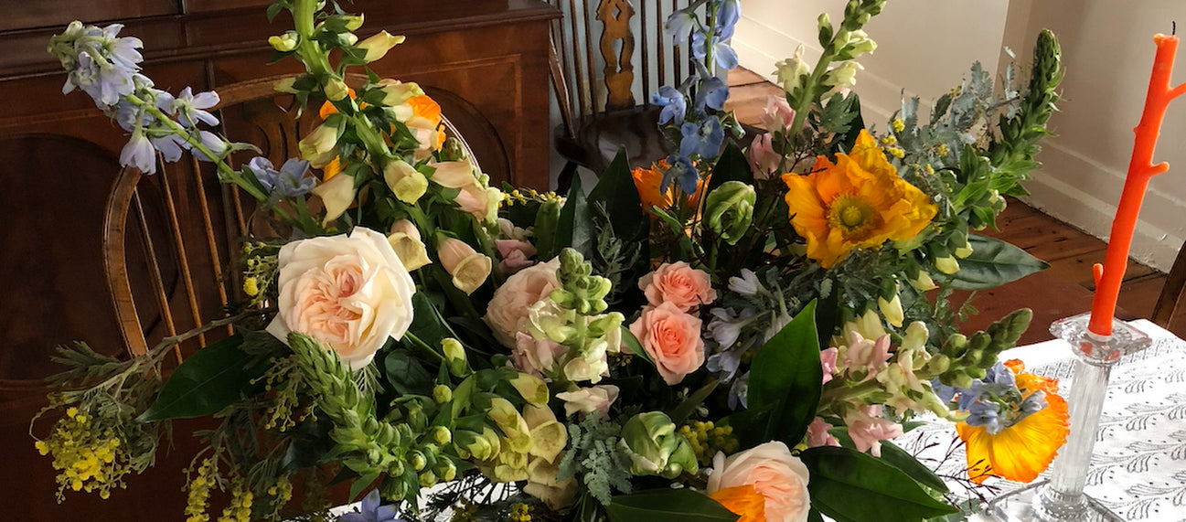 Floral arrangements on a table with a chair and tablecloth in the background