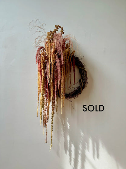 Decorative wreath with hanging strands on a white wall, labeled 'SOLD'.