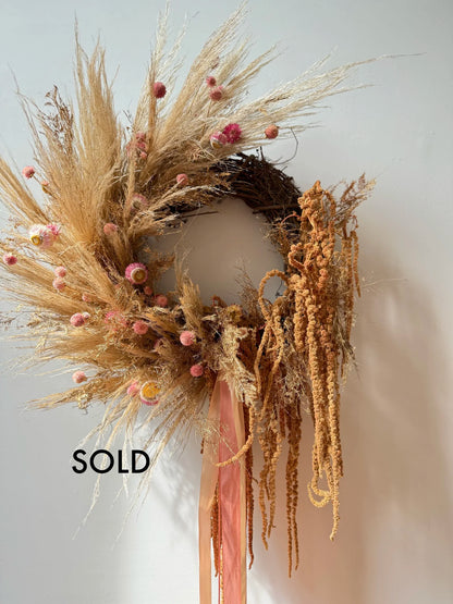 Decorative wreath with dried grasses and pink accents on a plain background